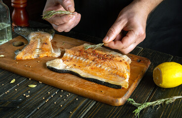 The cook adds rosemary to salmon steaks. The process of preparing a fish dish with spices by the hands of a chef in a restaurant kitchen.