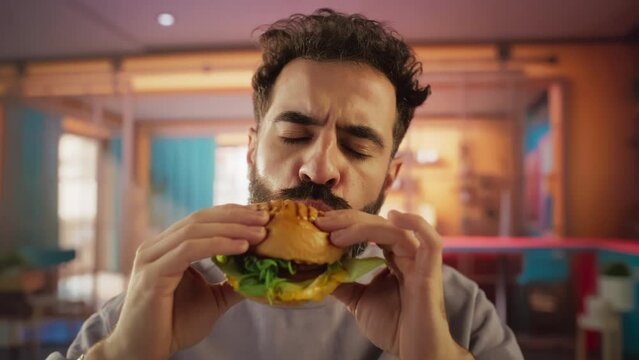Tracking Slow Motion Portrait of a Man Who is Enjoying a Delicious Hamburger at Home. Colorful Setting For a Happy Male Who Ordered Fast Food Delivery, Approving of the High Quality