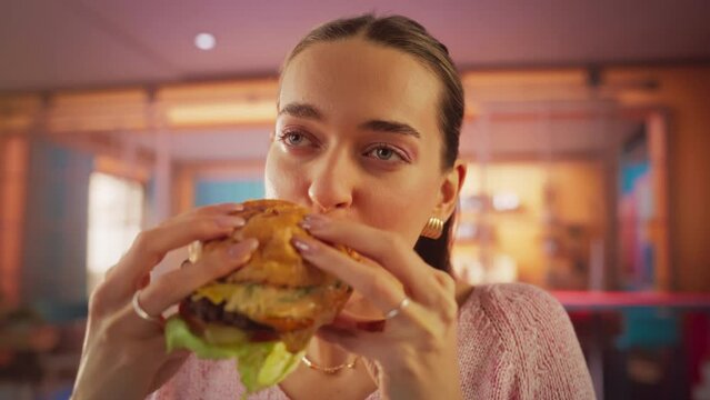 Tracking Slow Motion Portrait of a Woman Who is Enjoying a Delicious Hamburger at Home. Colorful Setting For a Happy Female Who Ordered Fast Food Delivery, Approving of the High Quality