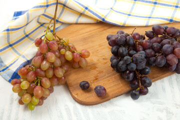 Cutting board with bunches of organic pink and dark blue grapes on white wooden background..