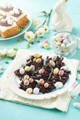Easter chocolate nest cake with mini chocolate candy eggs with blossoming cherry or apple flowers on blue background table. Creative recipe for Easter table with holiday decorations. Top view.