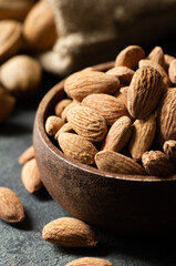 Delicious sweet almonds in wooden bowl or burlap sack on rustic background, roasted almond nut, healthy food
