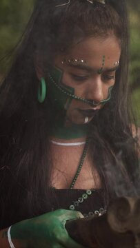 Focused young shaman woman in traditional Mayan attire performing a ritual smoking ceremony with a clay incense burning copal smoke in Mexico