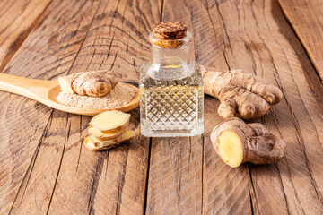 Homemade natural ginger root oil in bottle with a cork cap on a wooden background among ginger...