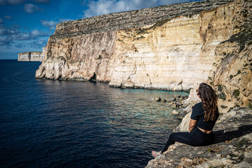 a person is sitting on top, edge of the cliff in Gozo, admiring the peaceful  sea view