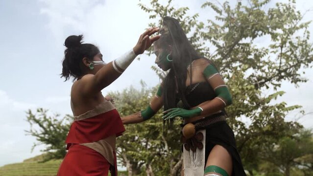 Confident young female Mayan warriors in traditional dress and body painting performing a traditional smoking ritual with incense copal burners in Mexico