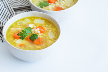 Chicken soup with vegetables and ptimtim - Israeli couscous, white background.