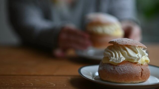 Coffee break with fresh traditional Swedish pastry, known as semla. In the background, out of focus, person eating semlor. Footage made in Sweden.