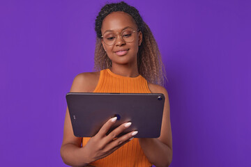 Young cute optimistic African American woman with electronic tablet in hands uses gadget to surf...