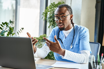 young jolly african american doctor with glasses consulting someone by phone and gesturing actively