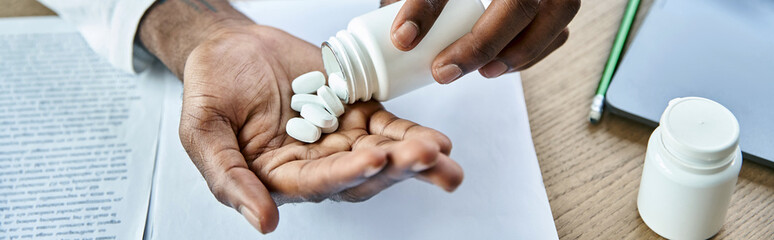 cropped view of young african american doctor pouring pills into hand at his office, banner