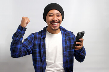 Excited Asian man, donning a beanie hat and casual shirt, raises his fist in a triumphant YES...