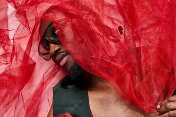 portrait of attractive african american man with red tulle fabric lying on floor, fashion concept