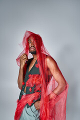 fashionable african american man posing with red tulle fabric and looking at camera, fashion concept
