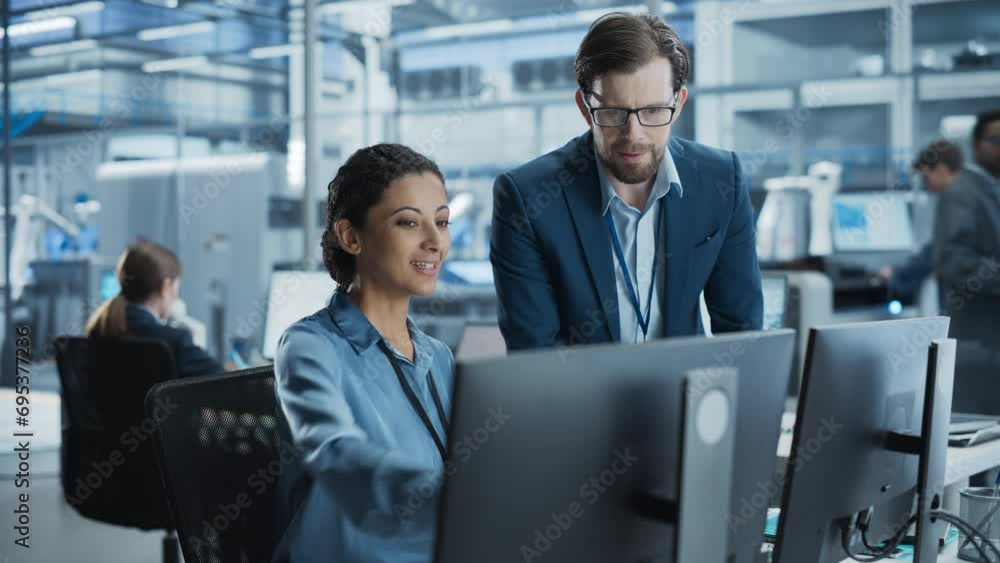 Poster Portrait of a Young Male Team Leader and Hispanic Female Engineer Collaborating on a Project, Using Computer and Talking in a Factory with Robotic Arms Producing Modern Devices for Tech Industries.
