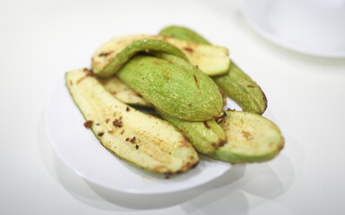 Close-up of baked delicious green zucchini. Juicy vegetable served on white plate with pepper. Tasty fresh vegs for healthy nutrition. Slices of courgettes. Cuisine and eating time concept