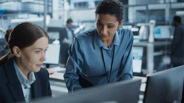 Caucasian Female Engineer And Hispanic Product Manager Using Desktop Computer And Talking At Automated Factory With Robotic Hands. Indian Facility Worker Using Soldering Jet Printer On Background.