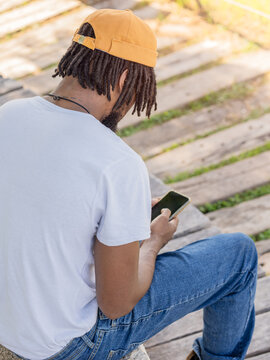Black guy with dreadlocks using cellphone in park