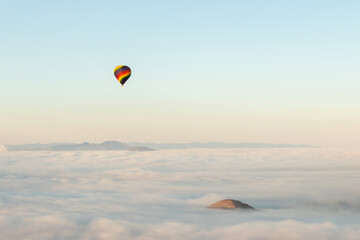 A solitary hot air balloon floats over a sea of clouds at sunrise, with a solitary peak of the Pyramid of the Sun emerging from the misty landscape of Teotihuacan, Mexico
