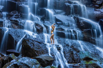 A young woman in a swimming suit at Nungnung waterfall in lush tropical forest, Bali, Indonesia