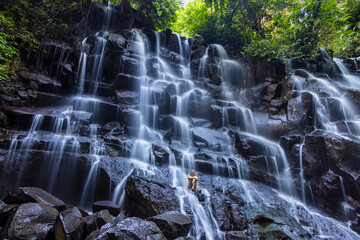 A young woman in a swimming suit at Nungnung waterfall in lush tropical forest, Bali, Indonesia