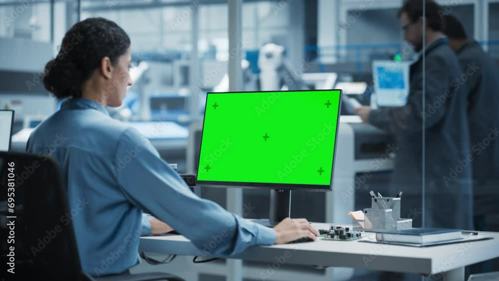 Fototapete Hispanic Female Robotics Engineer Using Desktop Computer with Green Screen Chromakey Mock Up Display in Factory Office. Technological Research and Development Facility with Autonomous Assembly Line.