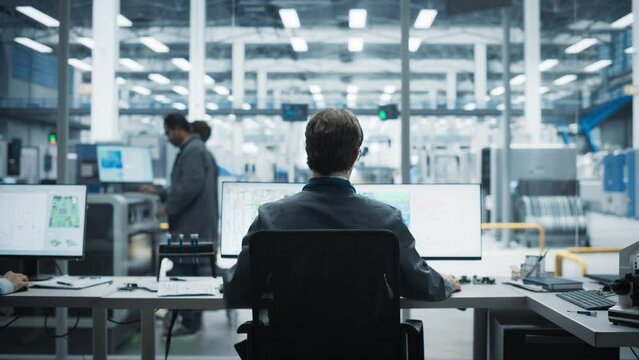 Backview Of Caucasian Male Industrial Engineer Working on Desktop Computer in Factory Office. Man Creating Innovative Motherboard with Powerful Microchips for Artificial Intelligence Systems.