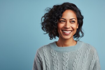 Fototapeta premium Portrait of a grinning indian woman in her 30s dressed in a warm wool sweater against a pastel blue background. AI Generation