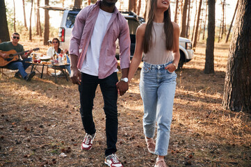 Couple are holding each other by the hands, walking. Group of friends are together in the forest