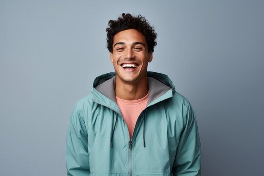 Portrait of a grinning man in his 20s wearing a lightweight packable anorak against a pastel gray background. AI Generation