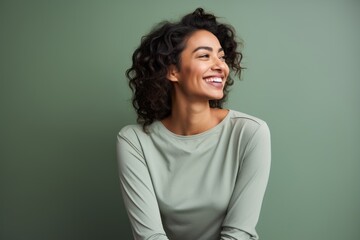 Obraz premium Portrait of a blissful indian woman in her 30s sporting a long-sleeved thermal undershirt against a soft green background. AI Generation