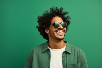 Portrait of a smiling indian man in his 20s wearing a trendy sunglasses against a soft green background. AI Generation