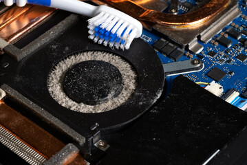 Dirty laptop computer fan is full of dust and needs cleaning using a toothbrush.