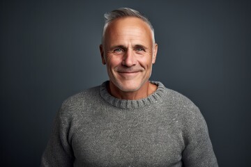 Obraz premium Portrait of a grinning man in his 50s wearing a cozy sweater against a soft gray background. AI Generation
