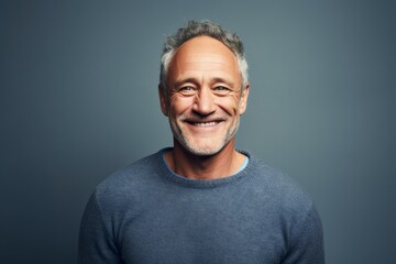 Portrait of a grinning man in his 50s wearing a cozy sweater against a soft gray background. AI Generation