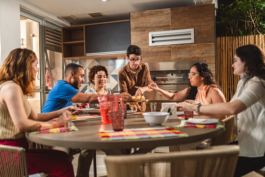 Homem jovem servindo seus convidados, na area de churrasco de sua casa.