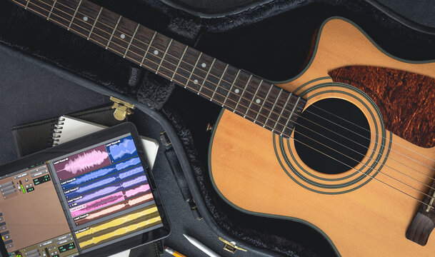 Acoustic guitar and digital tablet with a music application, top view.