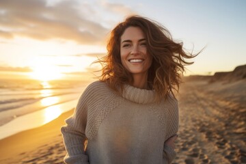 Portrait of a cheerful woman in her 30s dressed in a warm wool sweater against a stunning sunset beach background. AI Generation - obrazy, fototapety, plakaty