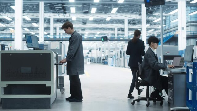 Printed Circuit Board Production At Electronics Factory: Asian Male Specialist Using Laptop, While Caucasian Engineer Printing Motherboards On Soldering Jet Printer. Computer Hardware Manufacturing.