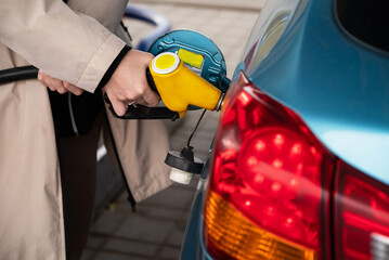 Attractive young woman refueling car at gas station. Female filling diesel at gasoline fuel in car using a fuel nozzle. Petrol concept. Side view - obrazy, fototapety, plakaty