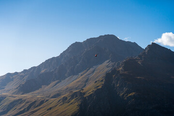 red helicopter flying toward the rocky Mont-Cenis mountain for rescue or security checks. blue sky and soft light