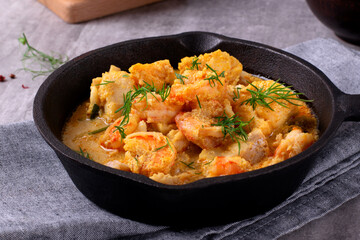 Fish curry with codfish, pollack and shrimps with coconut milk served in cast iron pan - 695406645