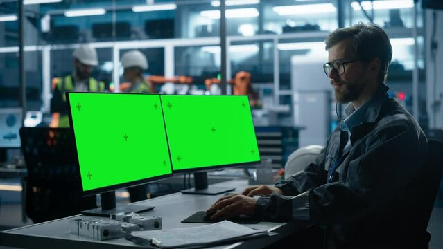 Caucasian Industrial Engineer Controlling Autonomous Conveyor With Robot Arms At Electric Engine Factory. Man Using Computer With Green Screen Chromakey On Display To Adjust Automated Production.