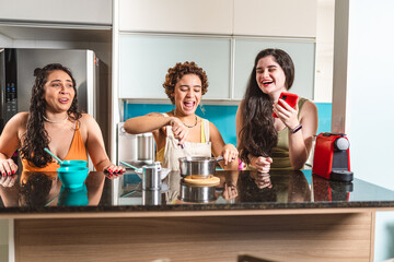 Mulheres jovens na cozinha se divertindo preparando uma receita juntas. - obrazy, fototapety, plakaty