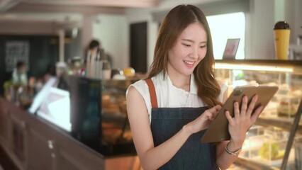 An Asian woman entrepreneur using tablet checking stock or sale income in modern coffee shop , concept small business - Powered by Adobe