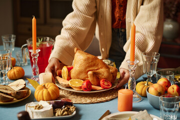 Unknown caucasian woman placing plate with roasted turkey in center of festive thanksgiving table