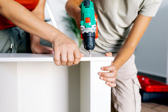 Anonymous mother with son fixing drawer with electric drill machine during moving