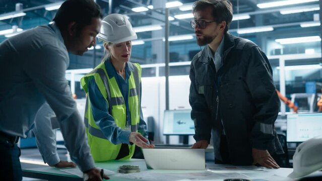 Young Diverse Team of Industrial Engineers Working in Office at Factory. Female Professional Technician Talks About Electric Engine Production. Autonomous Production Facility With Robotic Hands.