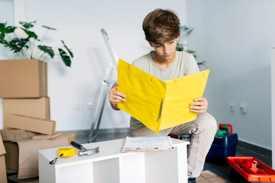 Focused boy kneeling and reading notes on yellow clipboard
