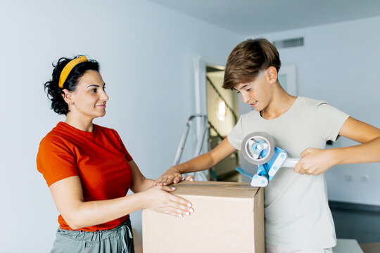 Boy packaging carton box with tape dispenser machine with mother holding box
